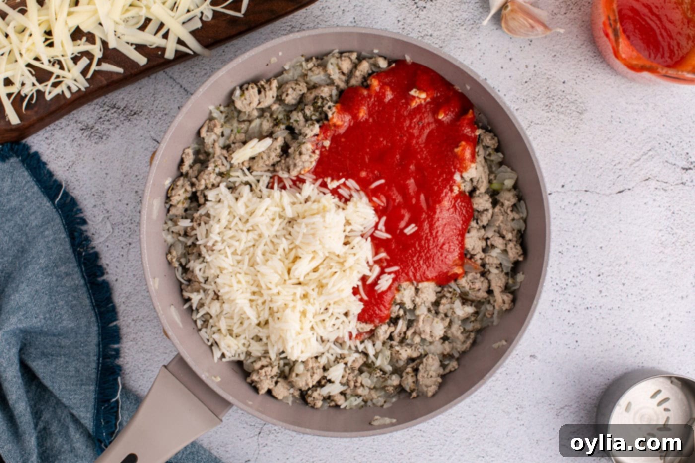 Strained tomatoes and cooked rice being stirred into the ground turkey mixture in a skillet, creating the flavorful filling.