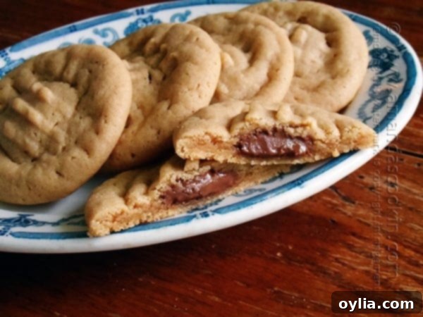 A close up of a Hershey drop stuffed peanut butter cookie split in half on a plate with whole cookies in the background.