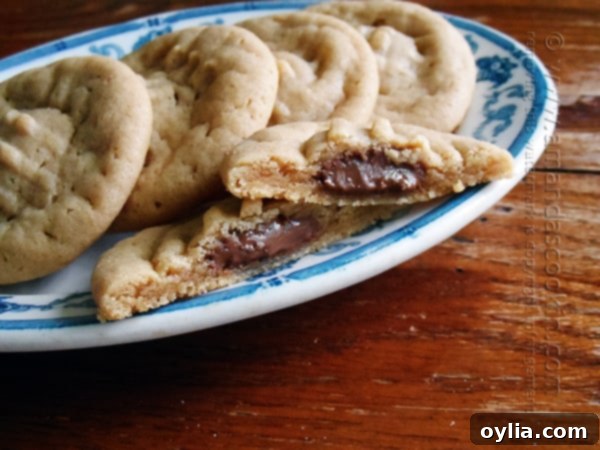 A close up of a Hershey drop stuffed peanut butter cookie split in half on a plate with whole cookies in the background.