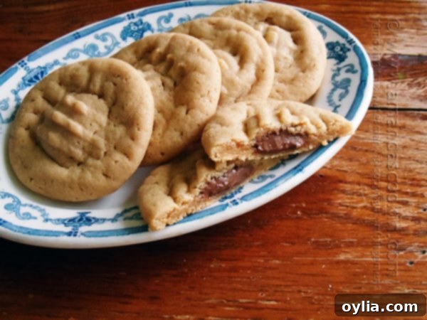 A close up of a Hershey drop stuffed peanut butter cookie split in half on a plate with whole cookies in the background.