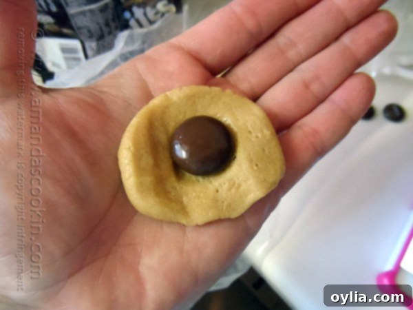 A photo of a hand holding flattened cookie dough with a Hershey drop on top.