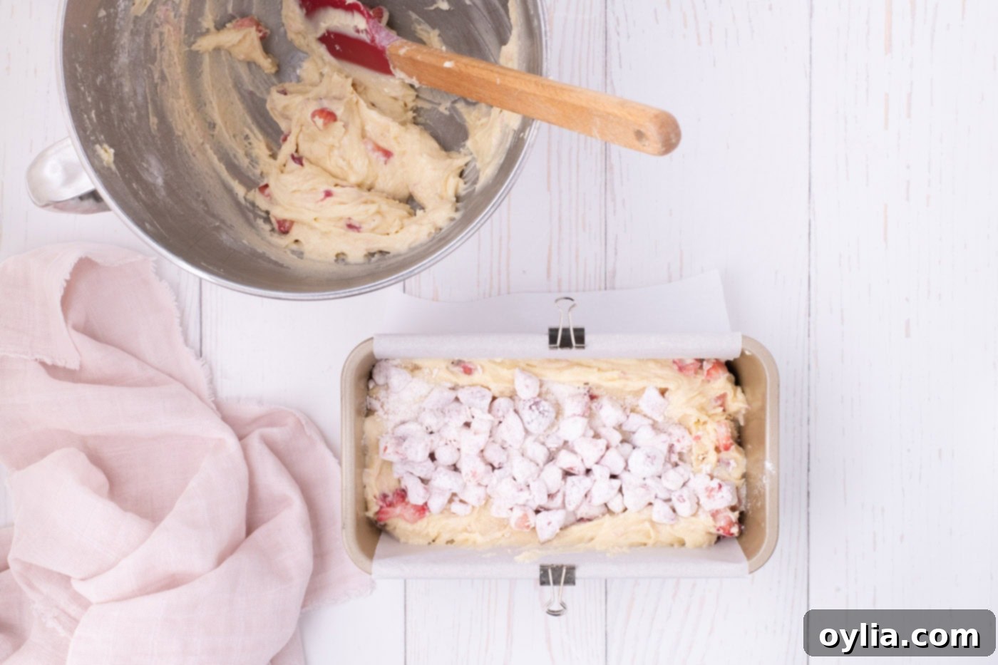 Strawberry pound cake batter in a loaf pan topped with a layer of strawberries, ready for the final batter.