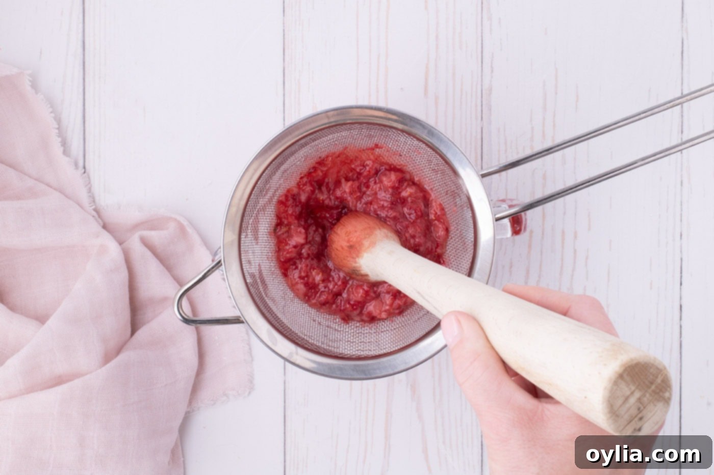 Muddling strawberries through a fine mesh sieve to extract juice for the glaze.