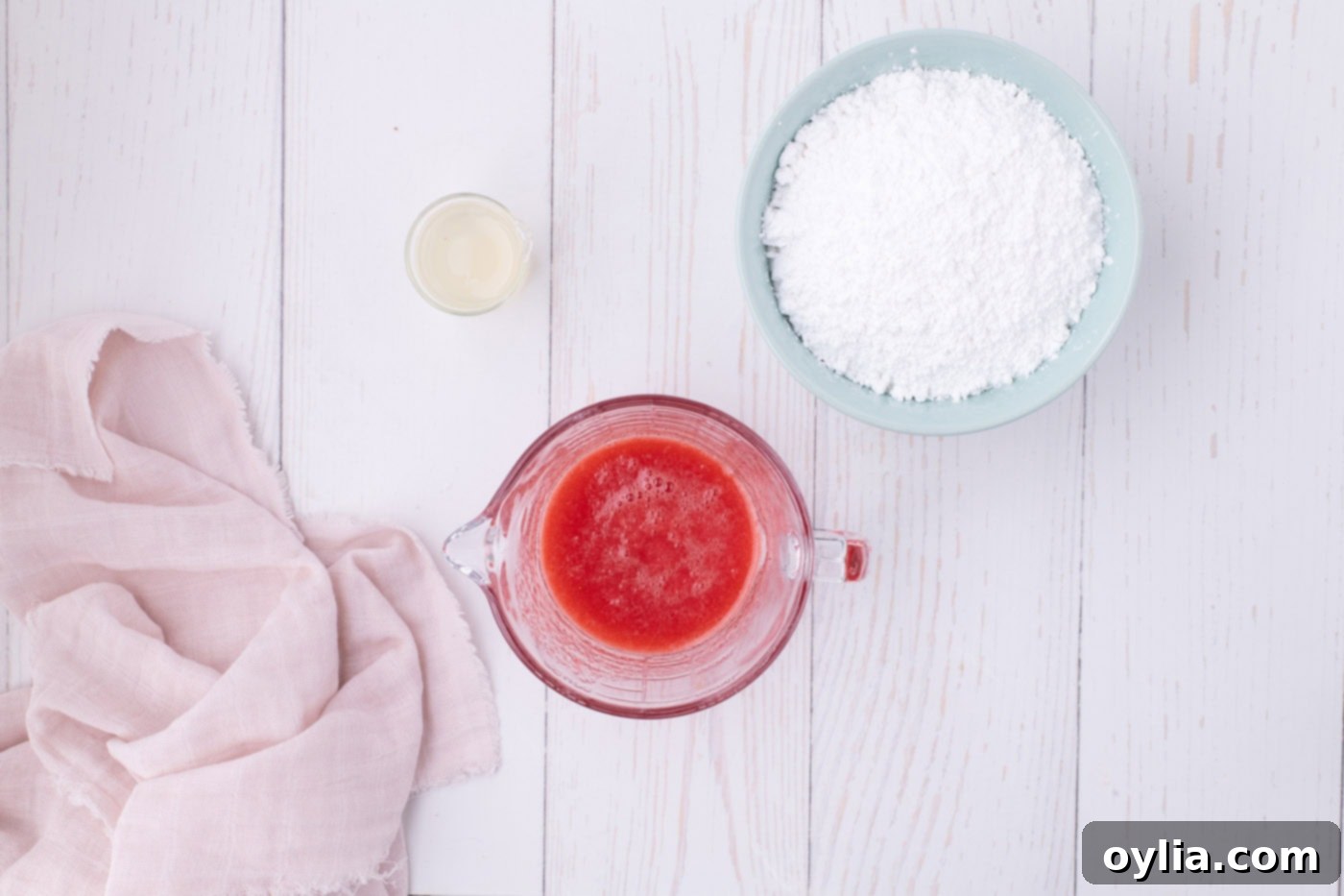 Strawberry juice in a measuring cup next to powdered sugar, ingredients for the glaze.