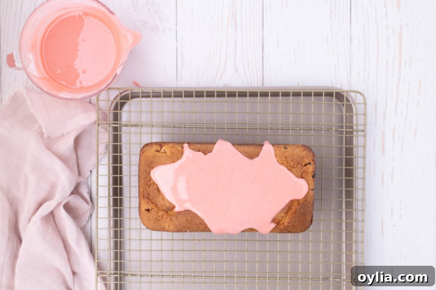 Strawberry glaze being poured over a pound cake, creating beautiful drips down the sides.