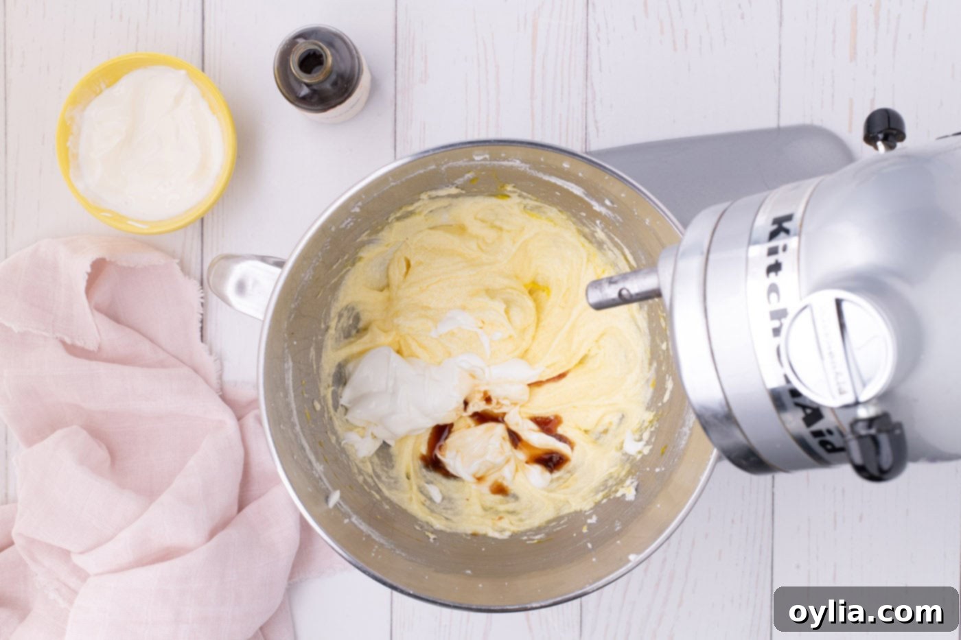 Adding vanilla and sour cream to the creamed butter and sugar mixture in a stand mixer, showcasing the smooth texture.