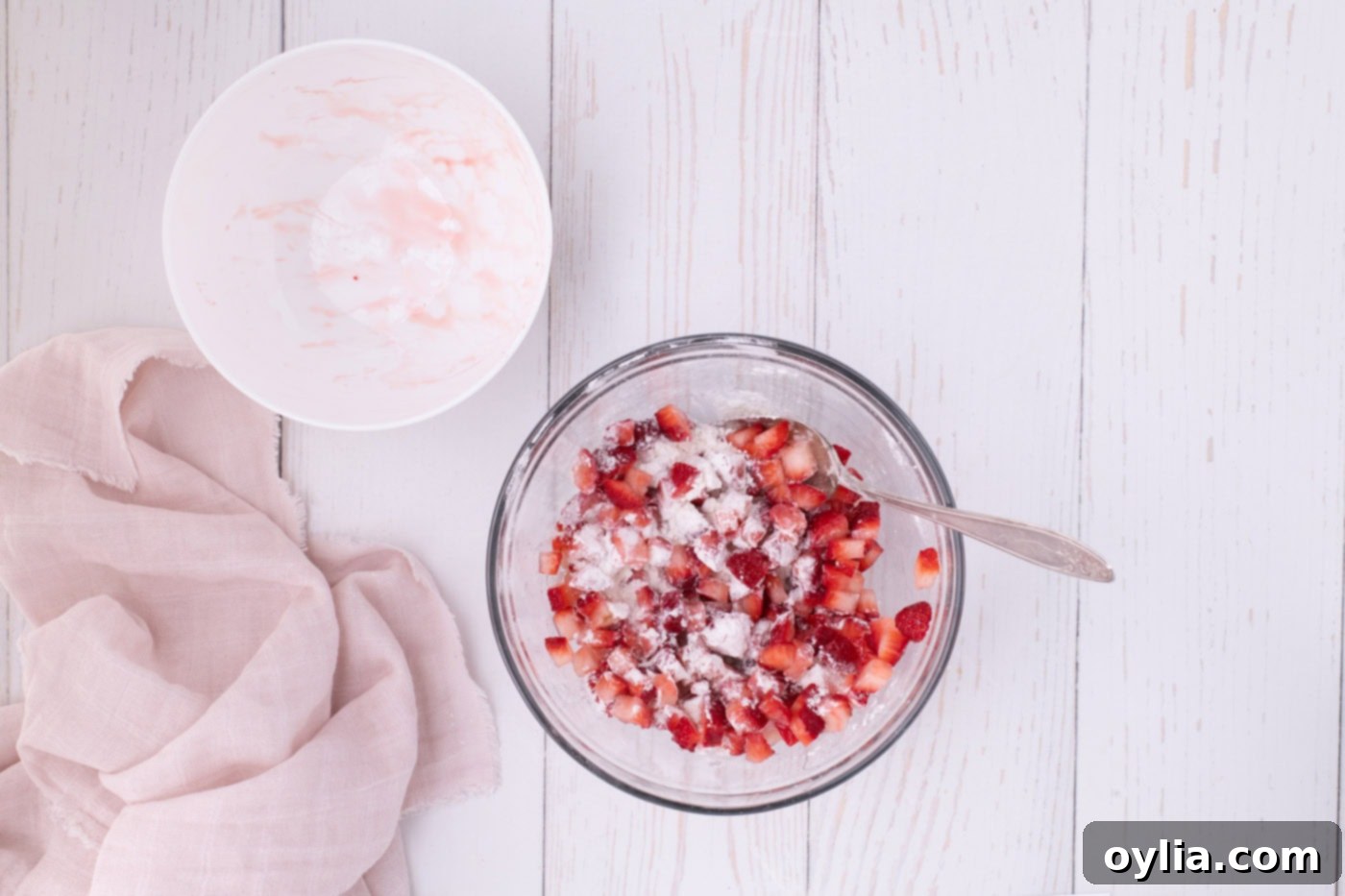 Diced strawberries mixed with lemon juice and then tossed with flour in a bowl, preparing them for the batter.