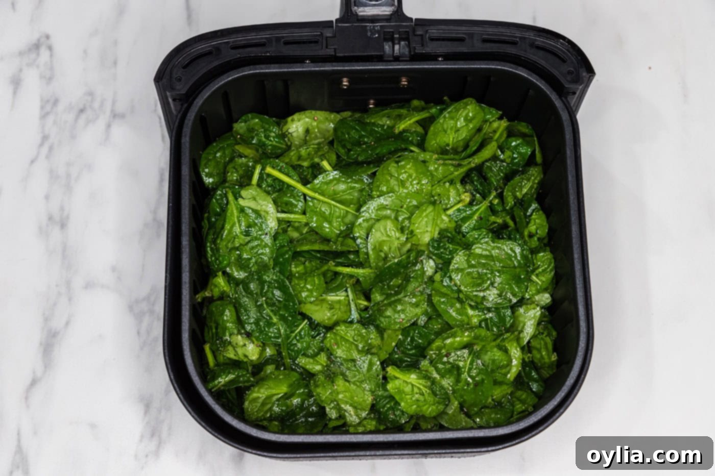 seasoned spinach leaves in an air fryer basket