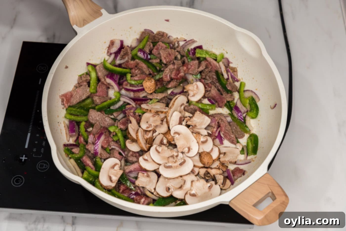 red onion, mushrooms, green bell peppers, and sliced steak cooking in a skillet
