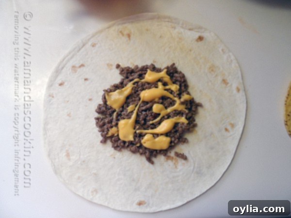 Warmed nacho cheese being drizzled over the seasoned ground beef layer on a tortilla.
