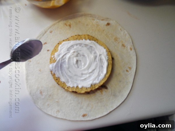 Sour cream being spread over a tostada shell, which is part of the Crunchwrap Supreme assembly.
