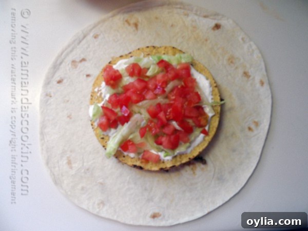 Shredded lettuce and diced tomatoes being sprinkled on top of sour cream on a tostada shell.