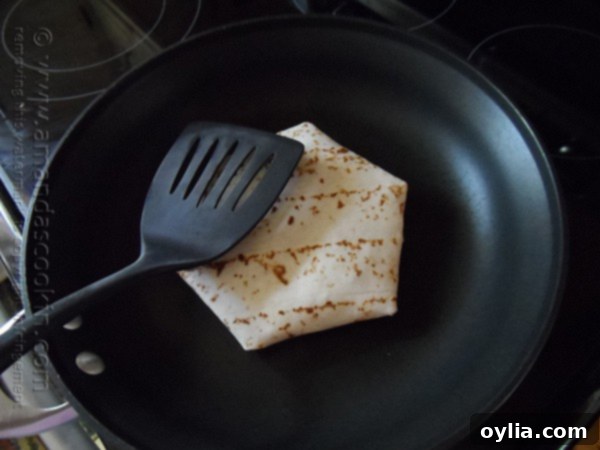 A homemade Crunchwrap Supreme cooking seam-side down in a hot skillet, browning evenly.