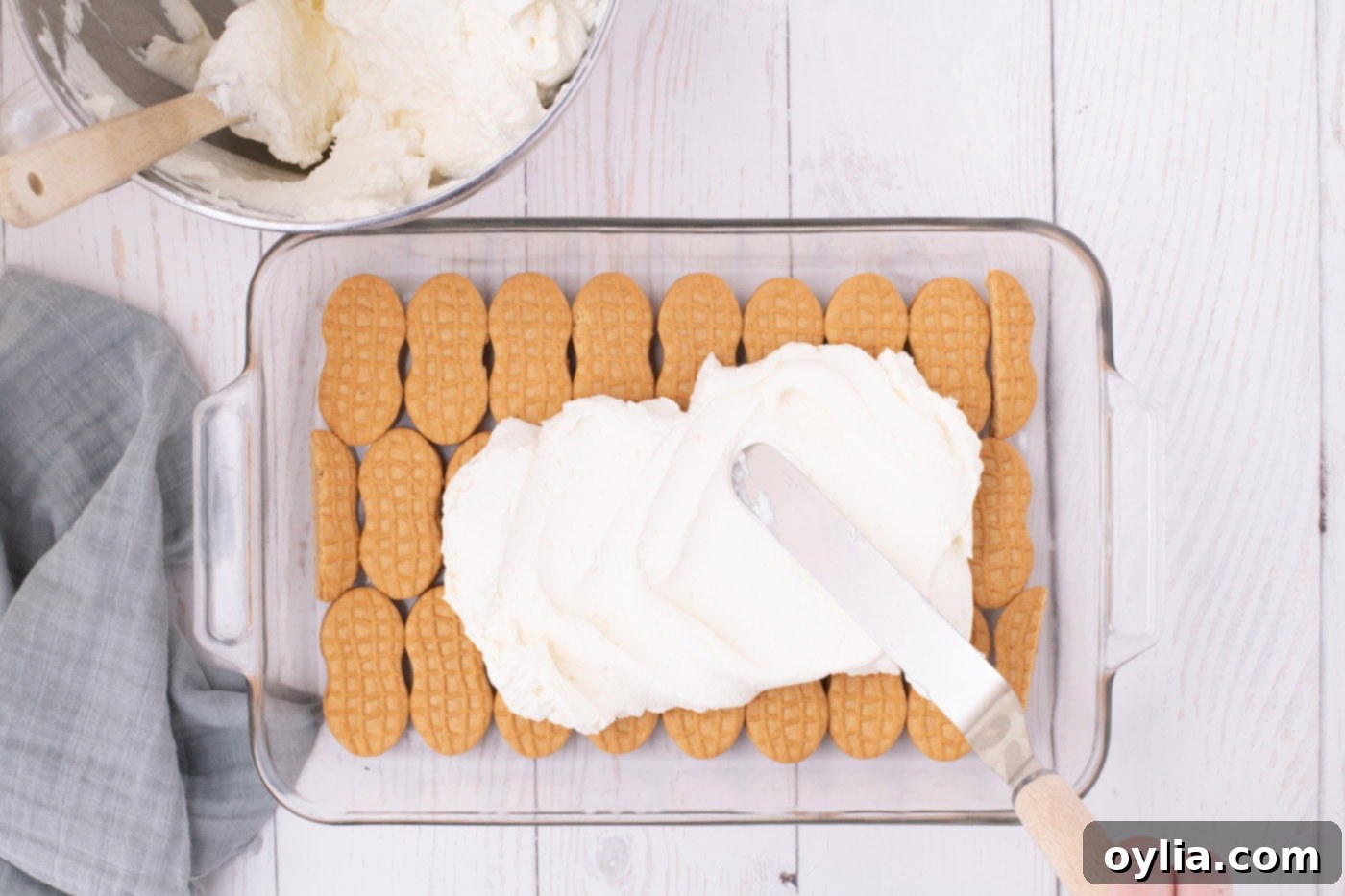 spreading whipped cream cheese layer over nutter butter cookies with an offset spatula
