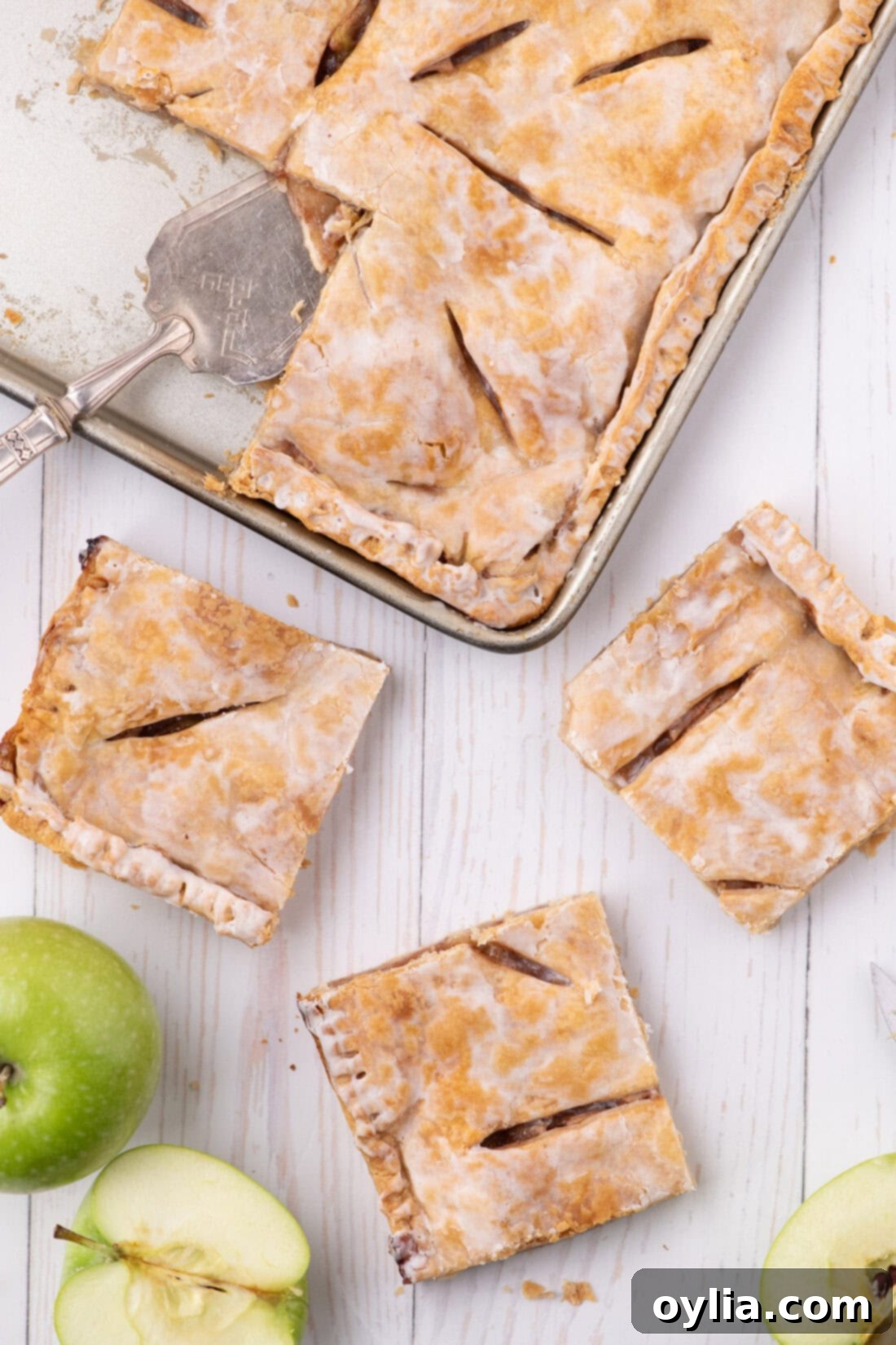Three slices of Apple Slab Pie resting on a table with the pan in the background, showcasing its golden, flakey crust and sweet apple filling, ready to serve a large crowd.