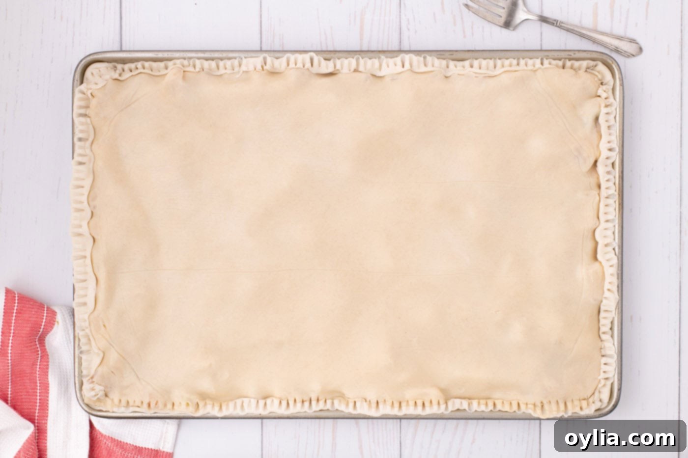 The edges of the apple slab pie crust are carefully crimped with a fork, creating a decorative and sealed border before baking.