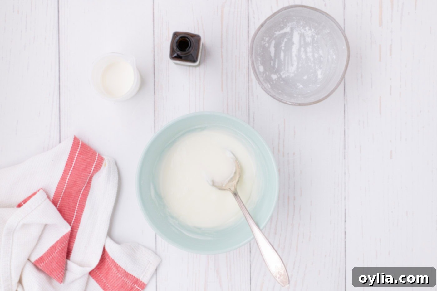 A bowl of smooth, white powdered sugar glaze with a spoon, ready to be drizzled over the baked apple slab pie.