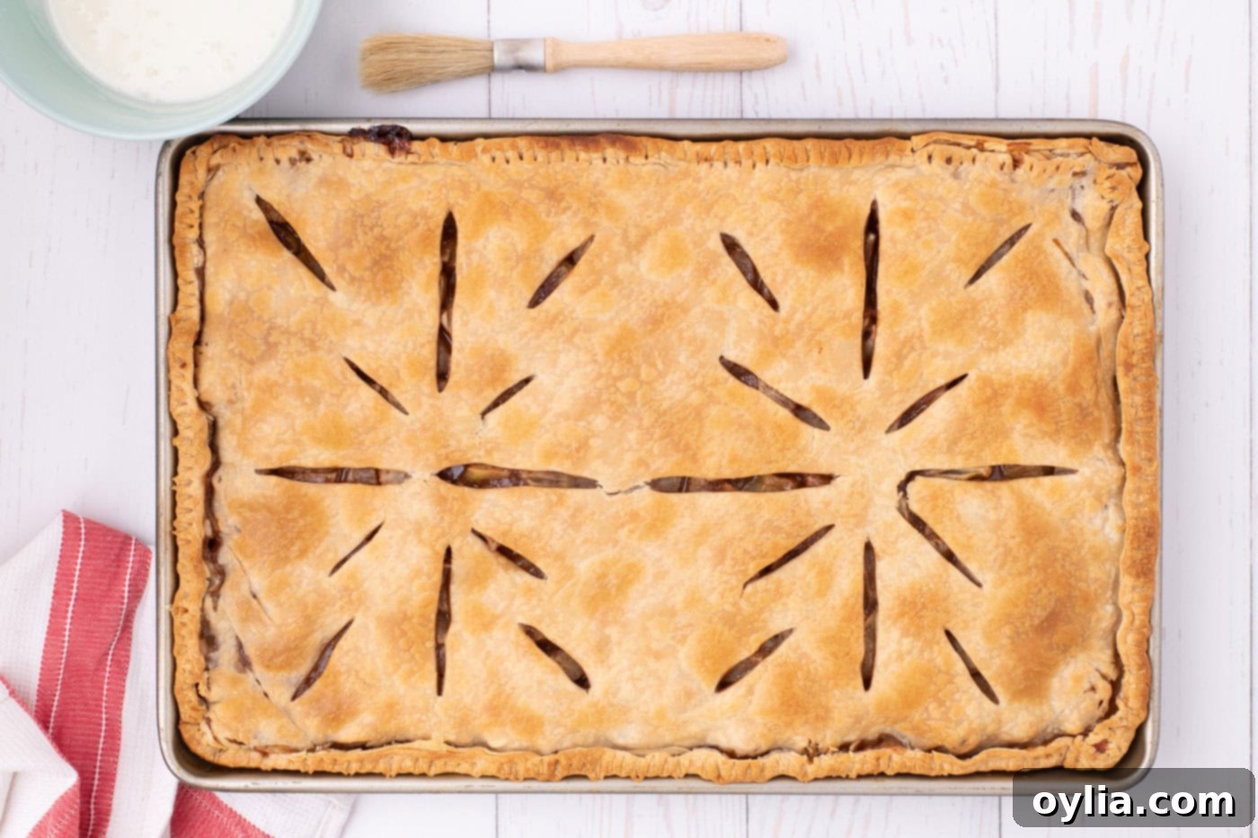 A freshly baked apple slab pie, golden brown and perfectly cooked, rests in a jelly roll pan on a wire rack, ready for its glaze.