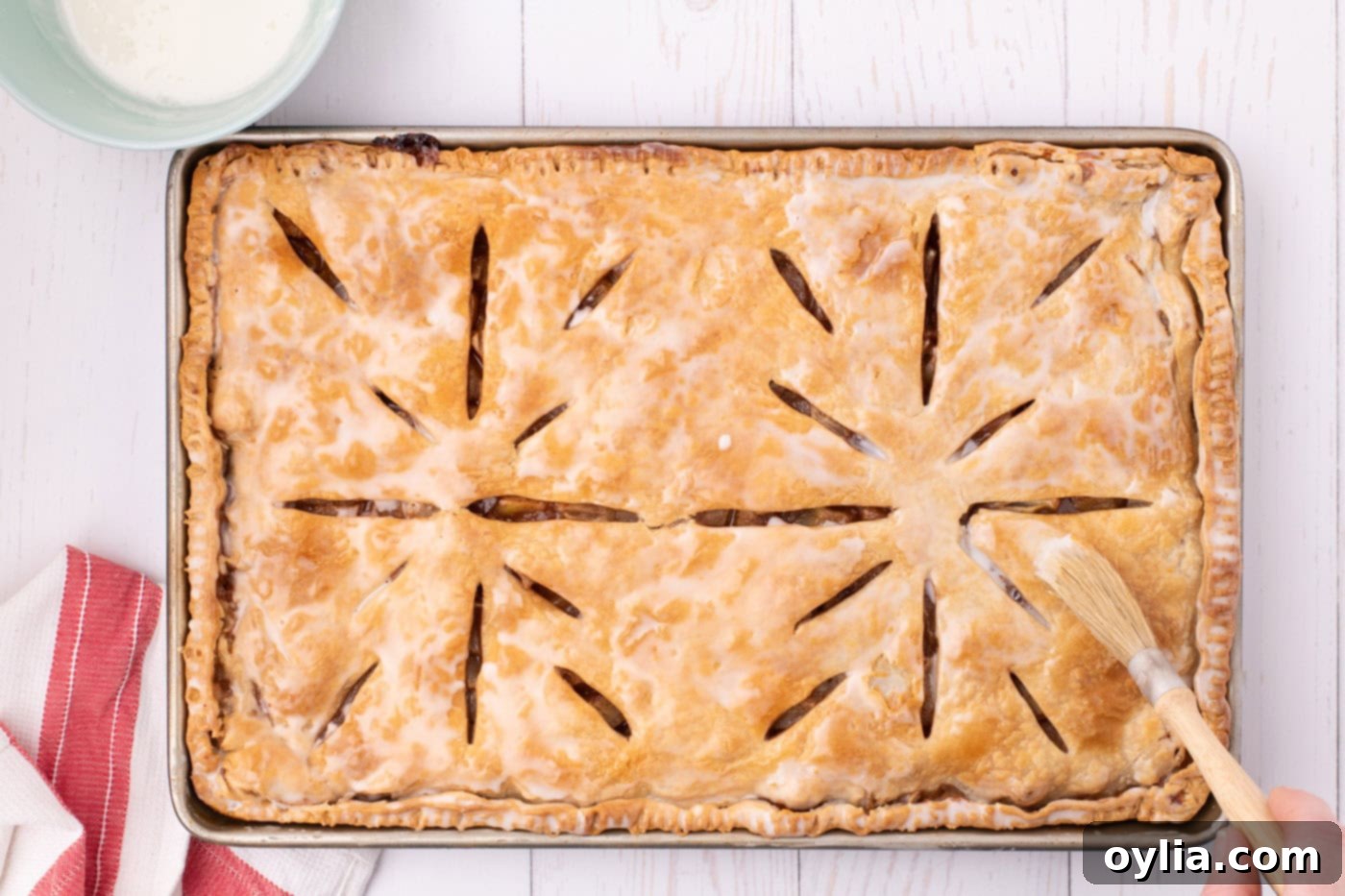 The baked apple slab pie, now glistening with a generous coating of smooth powdered sugar glaze, enhancing its appeal and flavor.