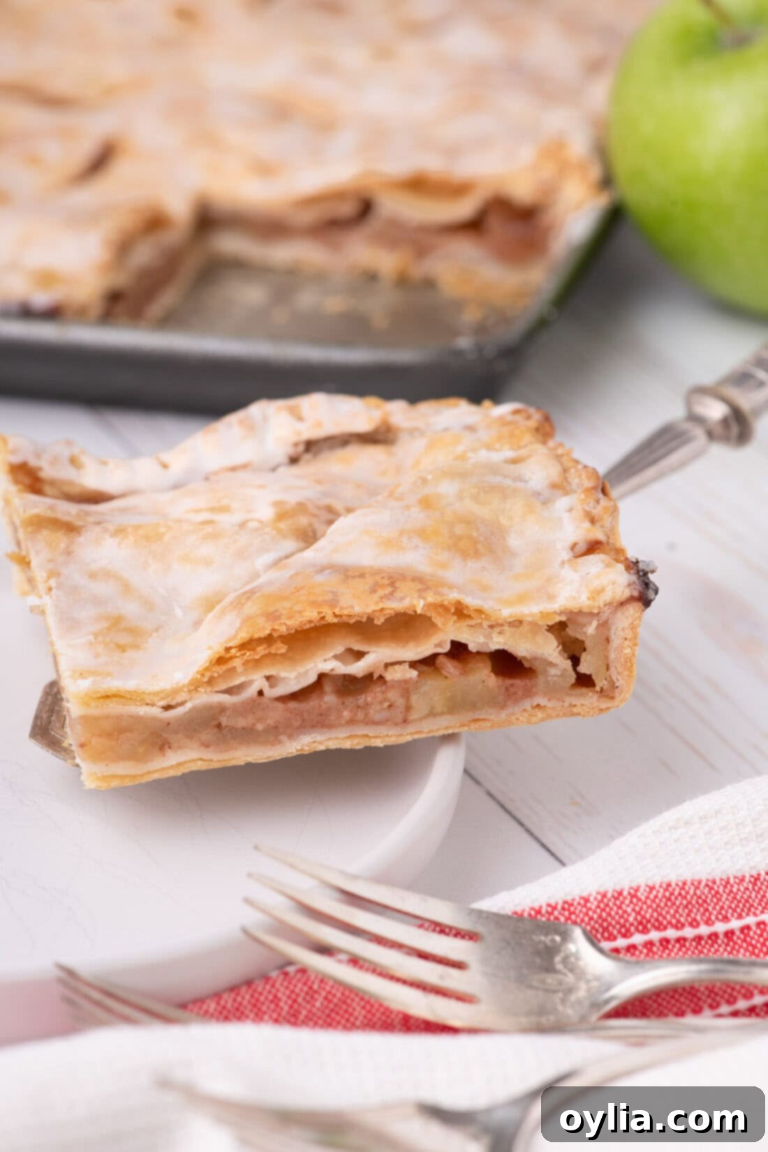 A perfectly baked slice of Apple Slab Pie on a white plate, showing the layers of golden crust and tender apple filling, ready to be enjoyed.
