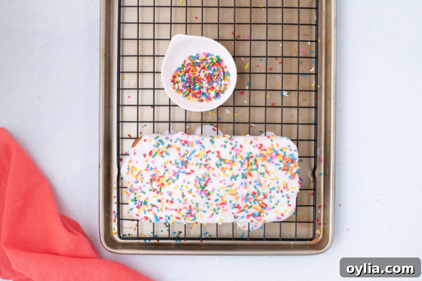 Ice cream bread with glaze and sprinkles cooling on a wire rack over a baking sheet