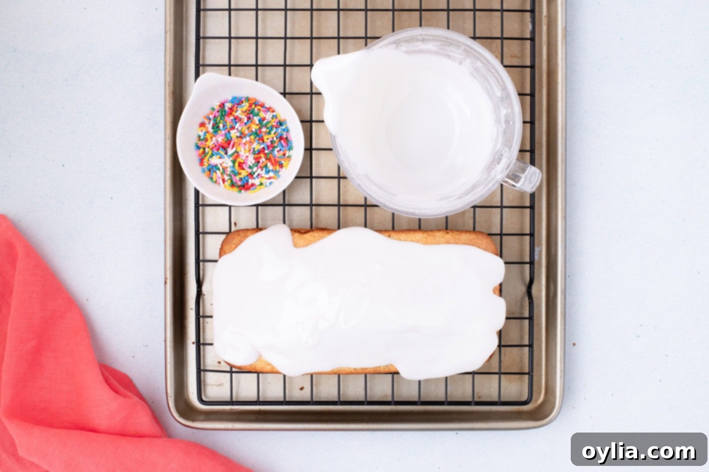 Vanilla glaze poured over a quick bread loaf, with a bowl of sprinkles on the side
