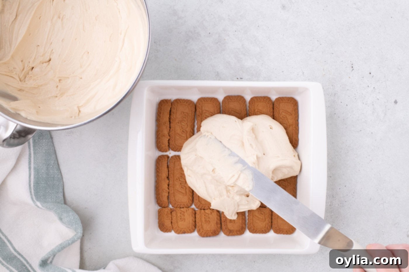 spreading Biscoff cream cheese mixture over cookies in a baking dish