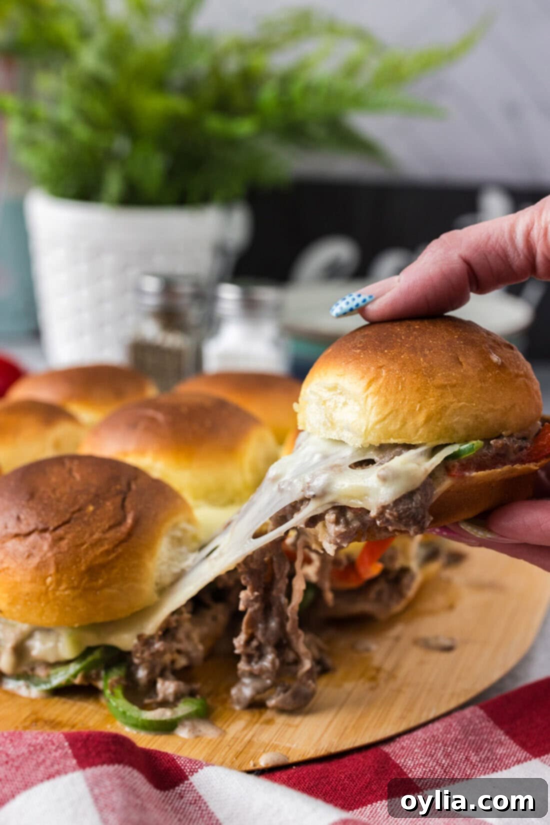 Hand pulling up a cheesy Philly Cheesesteak Slider from the board of Philly Cheesesteak Sliders