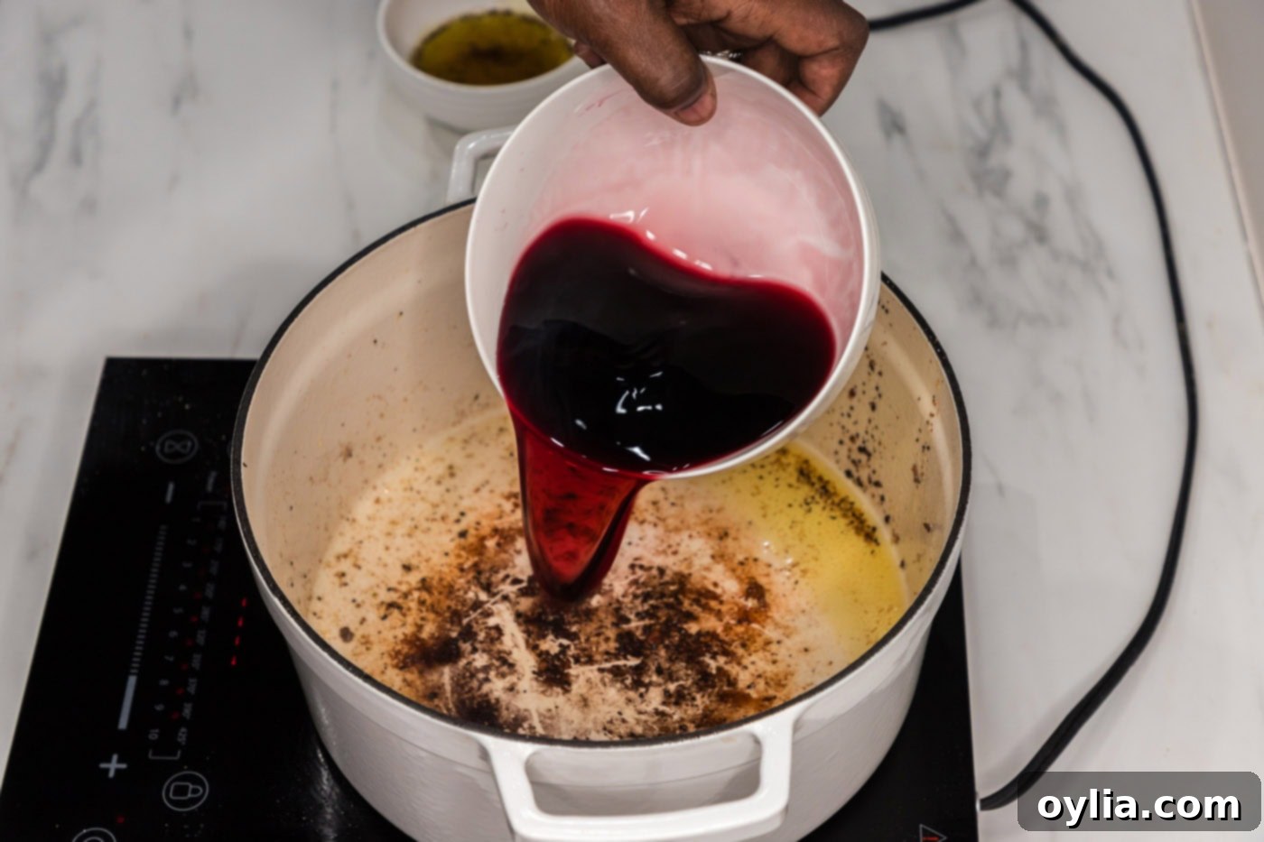 pouring red wine into a Dutch oven to deglaze the pan after browning oxtail.