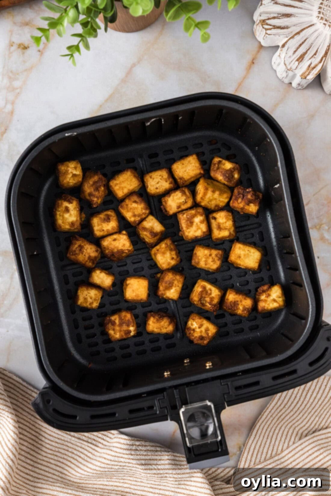 Crispy air-fried tofu cubes resting in an air fryer basket, showing their golden brown perfection.