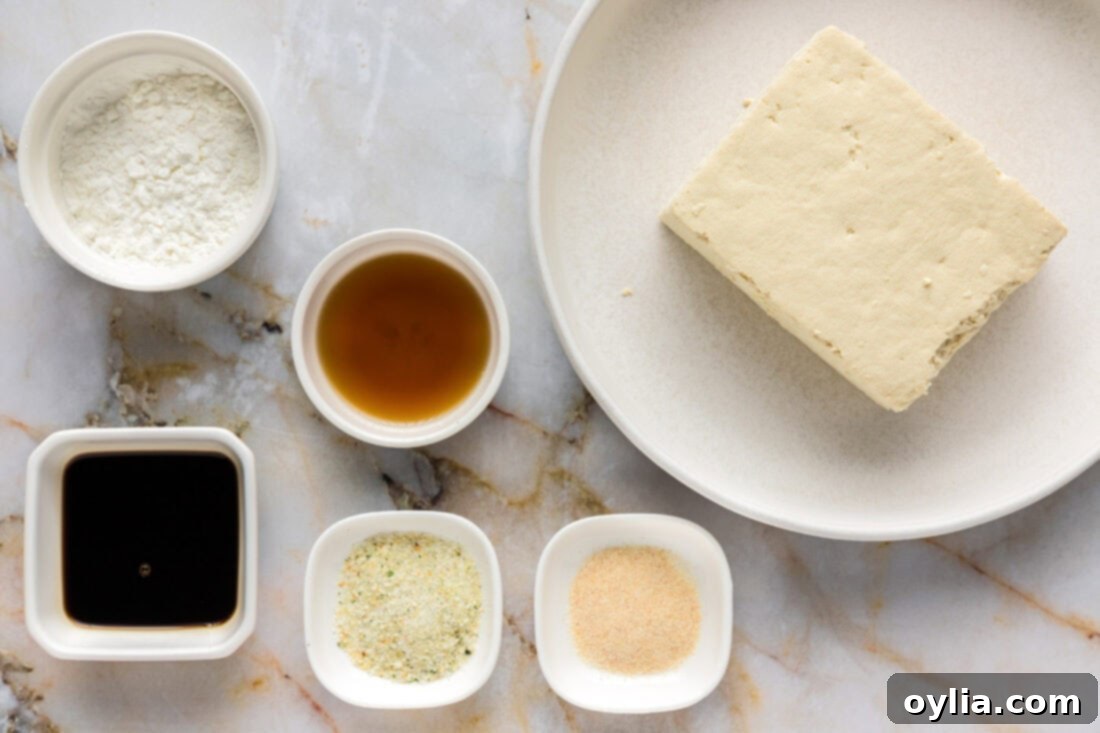 A collection of ingredients laid out, including a block of tofu, spices, cornstarch, soy sauce, and sesame oil, ready for making air fryer tofu.
