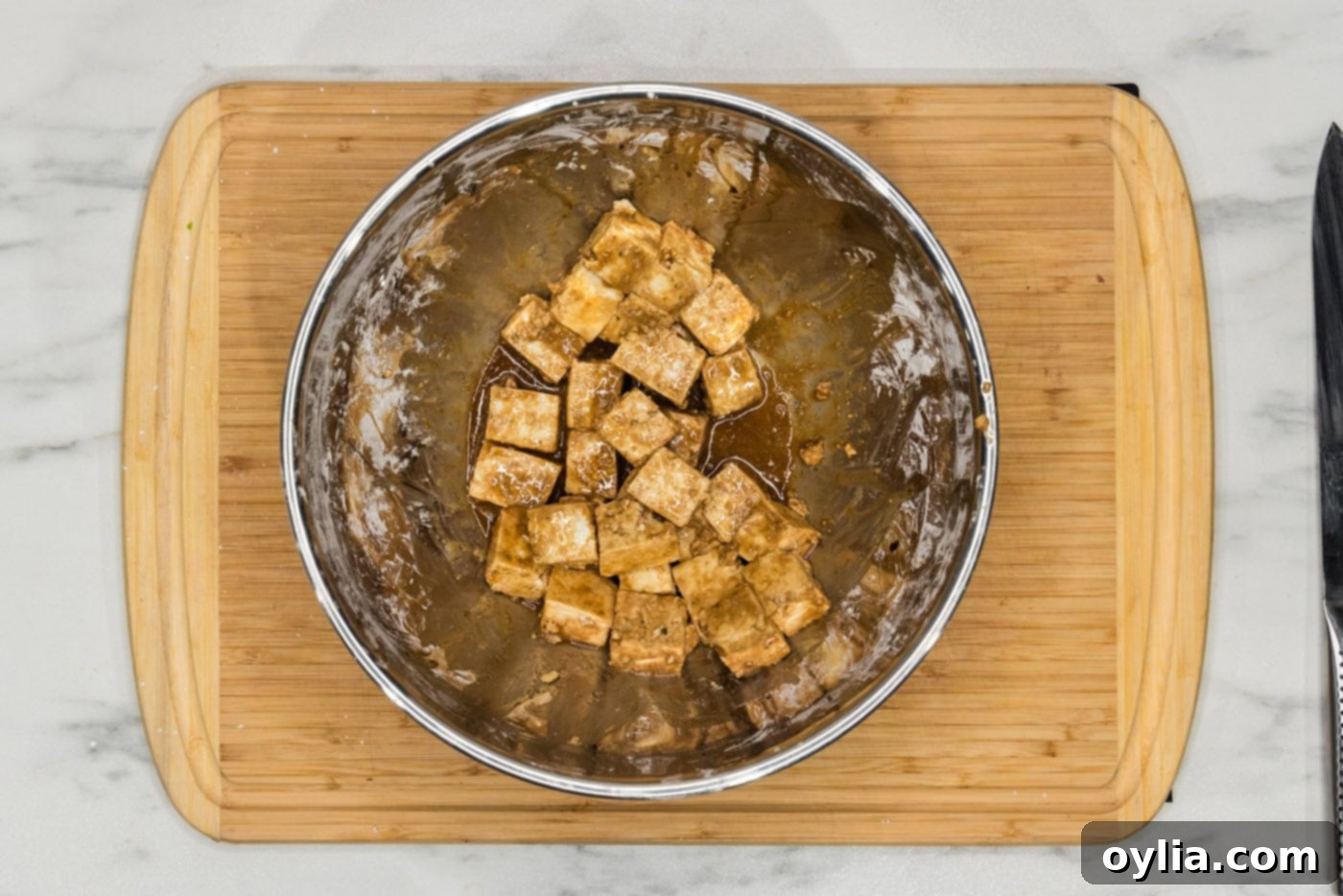 Cubed tofu in a bowl, now coated with soy sauce, cornstarch, and sesame oil, showing a uniform marinade.