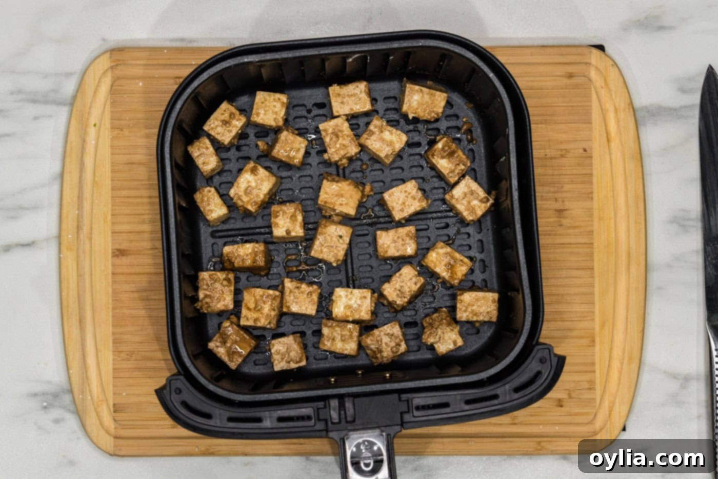 Seasoned tofu cubes arranged in a single layer in an air fryer basket, ready for cooking.