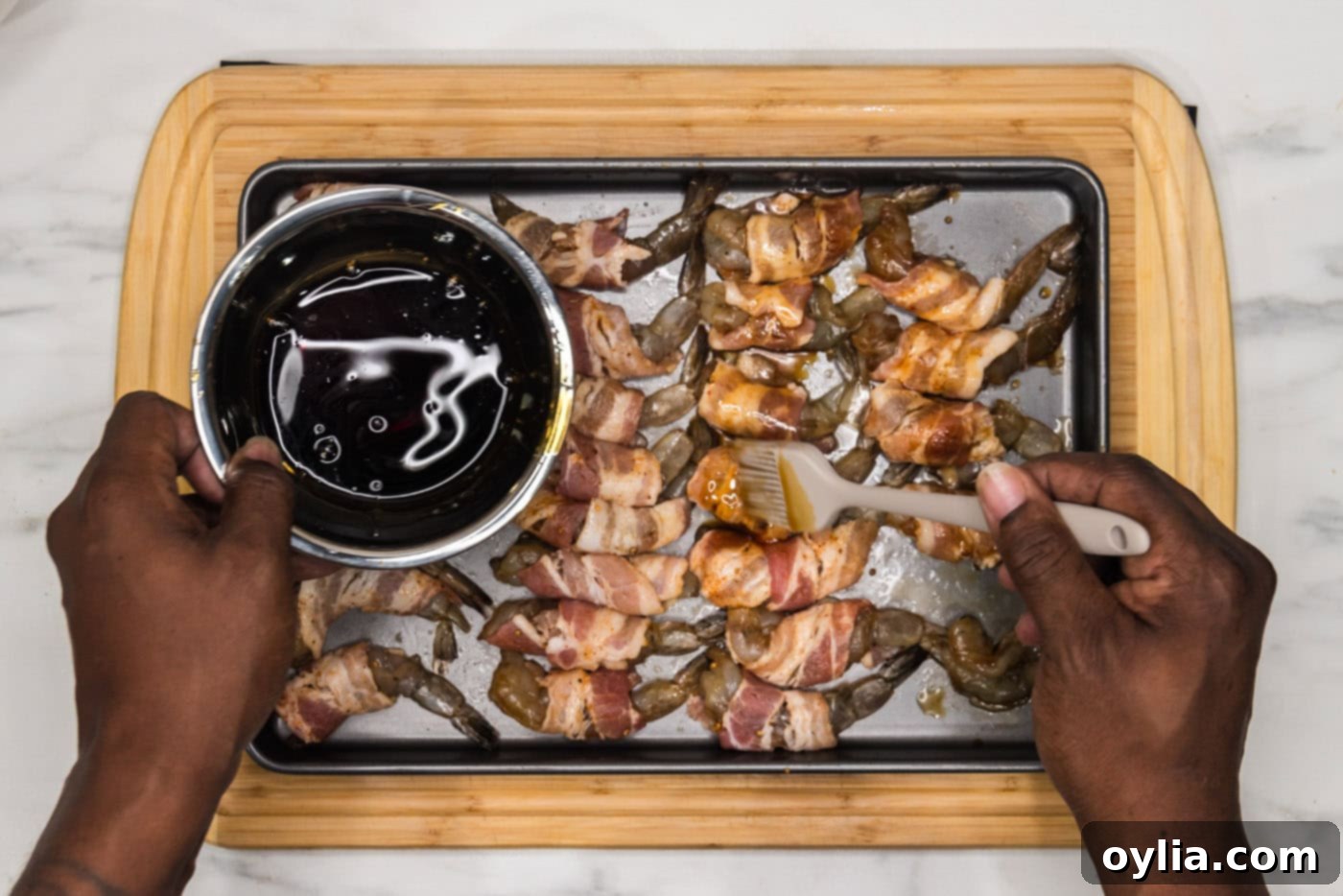 pouring soy sauce mixture over bacon wrapped shrimp on a baking sheet