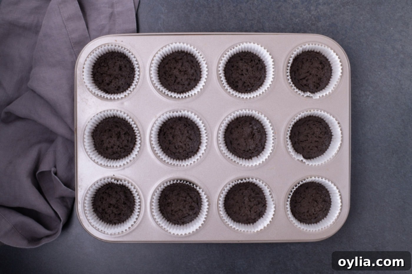 Baked Oreo cookie crusts cooling inside cupcake liners in a muffin pan