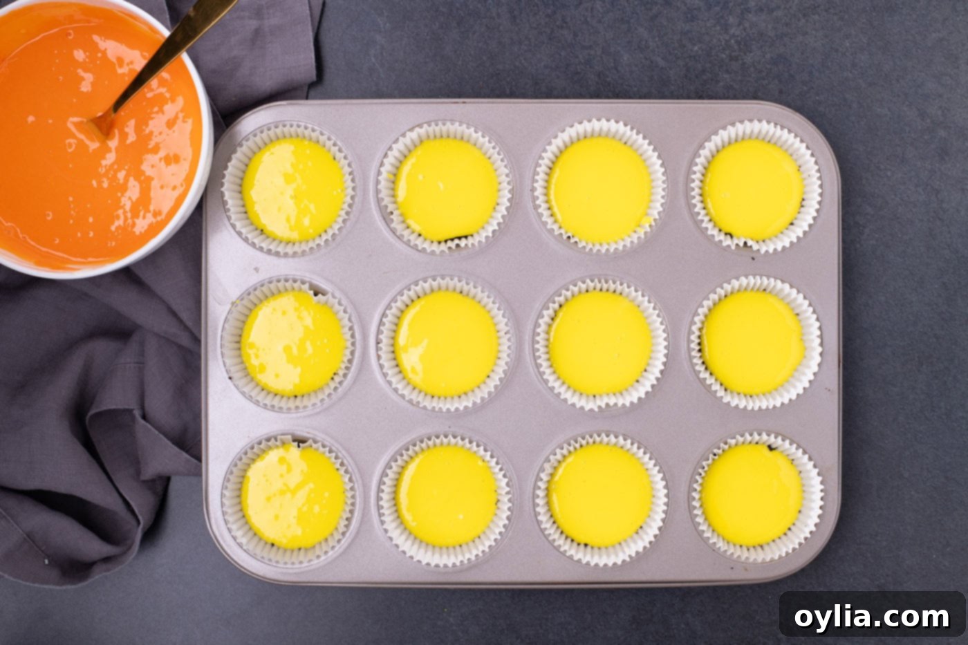 Yellow cheesecake batter carefully spooned onto Oreo crusts in a muffin pan