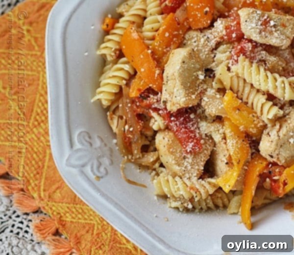 A close up overhead photo of chicken with peppers and pasta in a white bowl topped with Parmesan cheese.