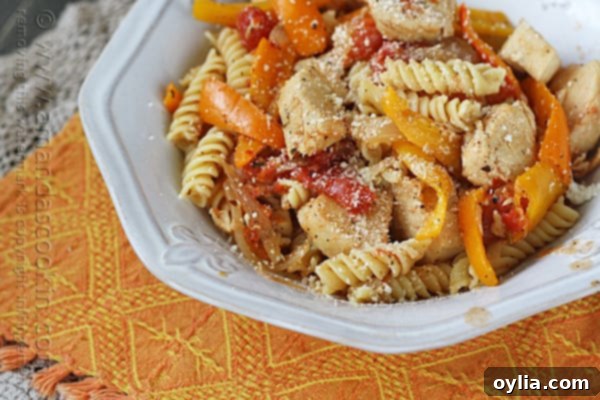 A close up photo of chicken with peppers and pasta in a white bowl topped with Parmesan cheese.