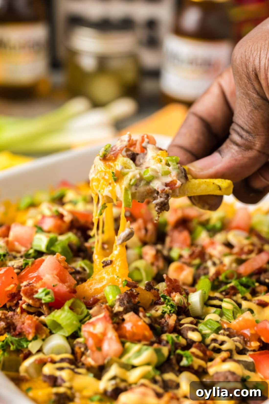 Hand holding a chip full of delicious, creamy Cheeseburger Dip garnished with fresh toppings.