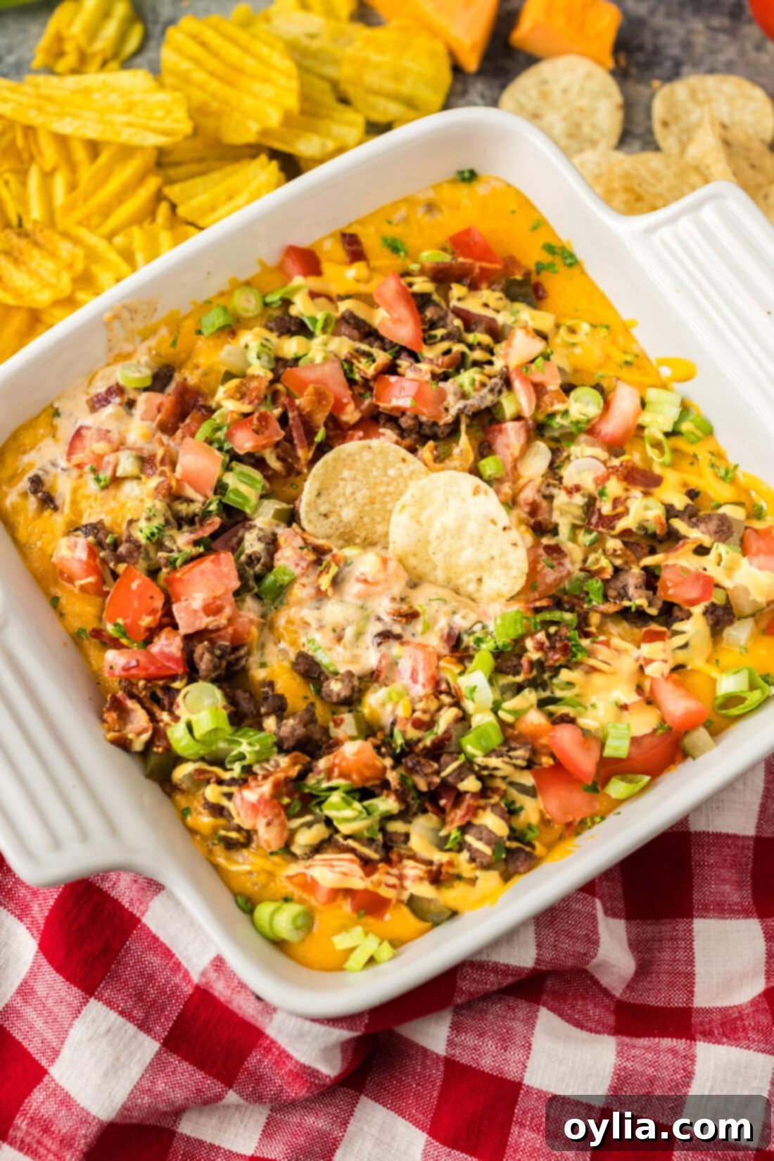 A baking dish filled with golden-brown, bubbly Cheeseburger Dip, with two tortilla chips ready for dipping.