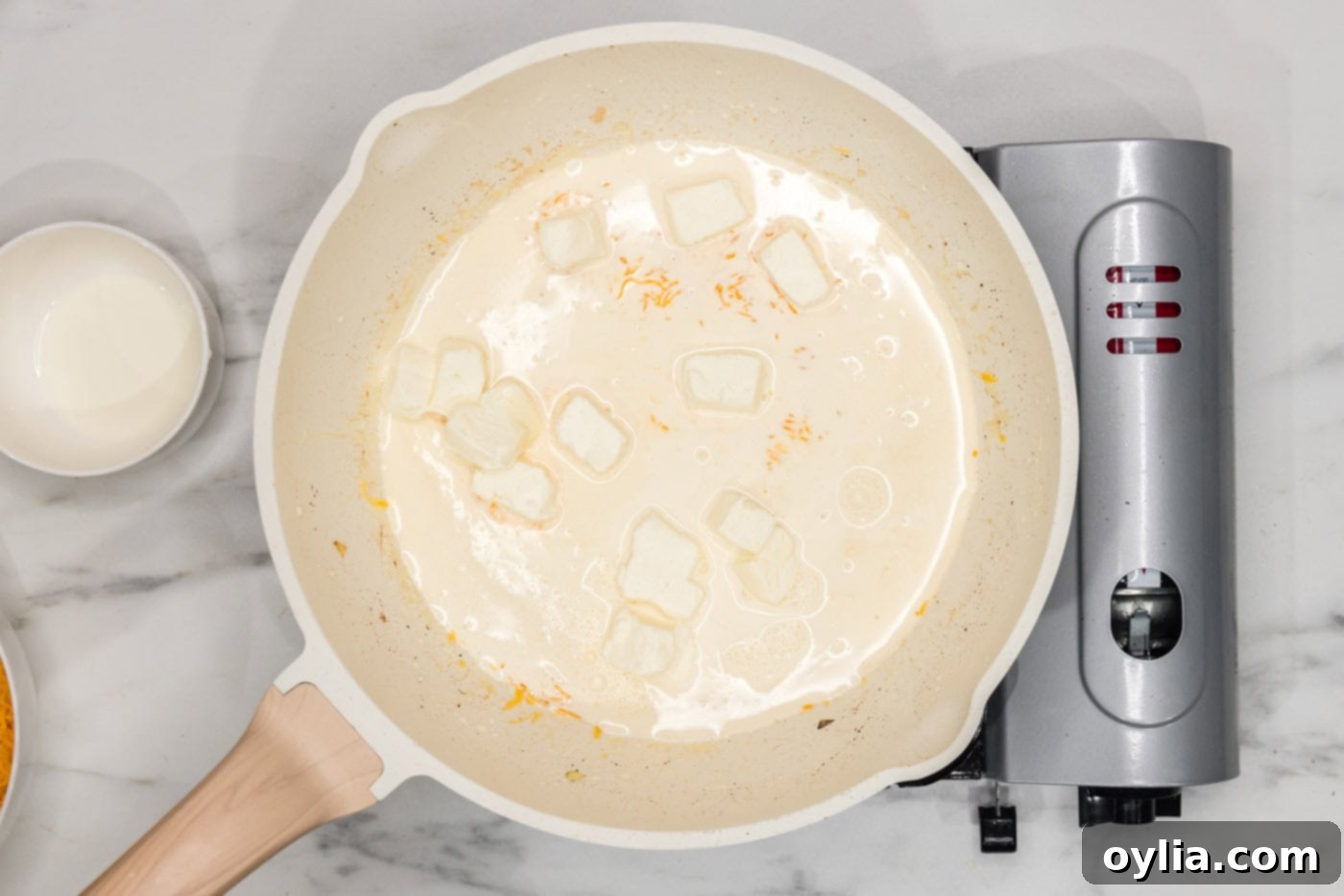 Softened cream cheese, heavy cream, and shredded cheddar melting together in a skillet, beginning to form a smooth sauce.
