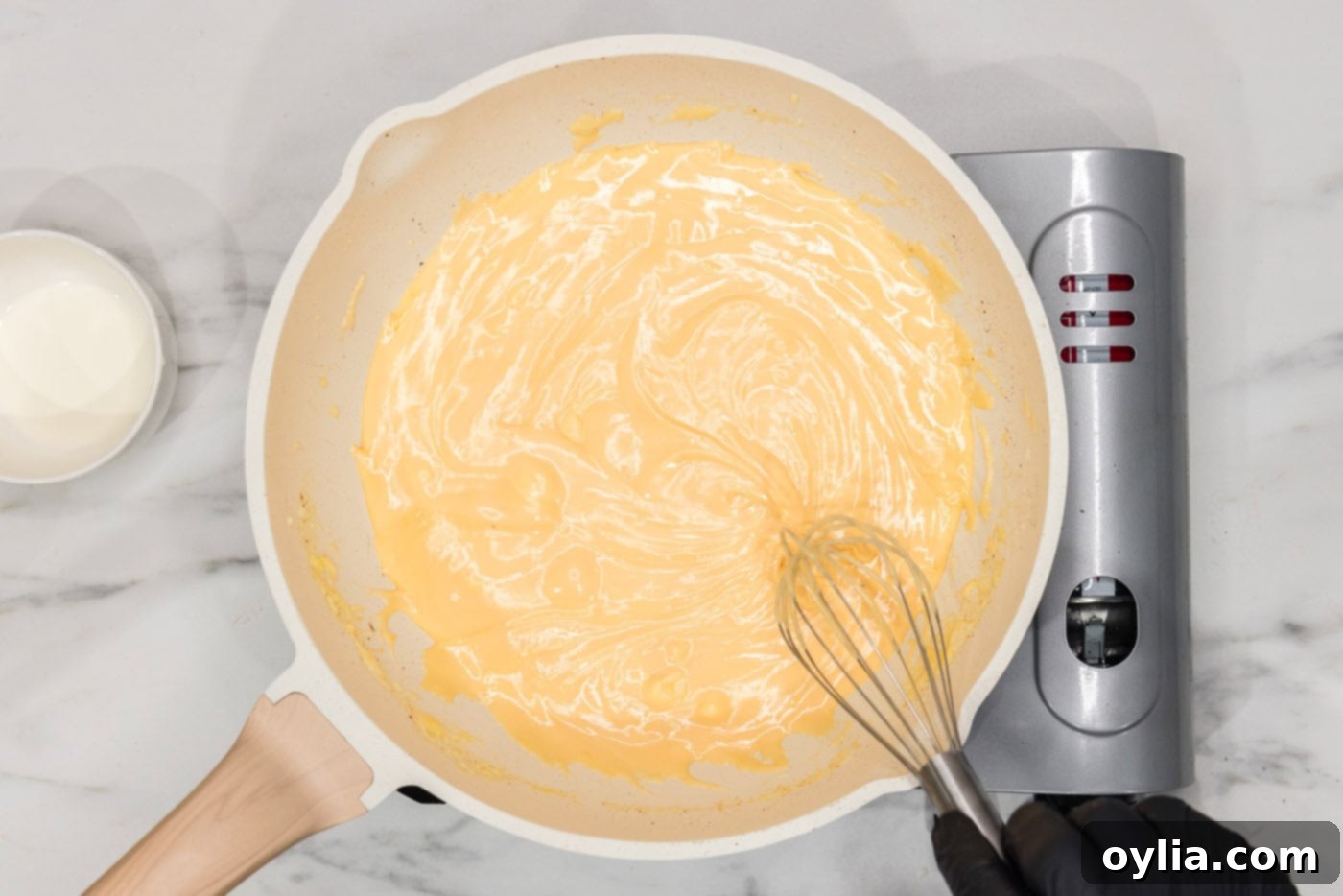 Continuously whisking the cheese sauce in a skillet until it is perfectly smooth and lump-free.