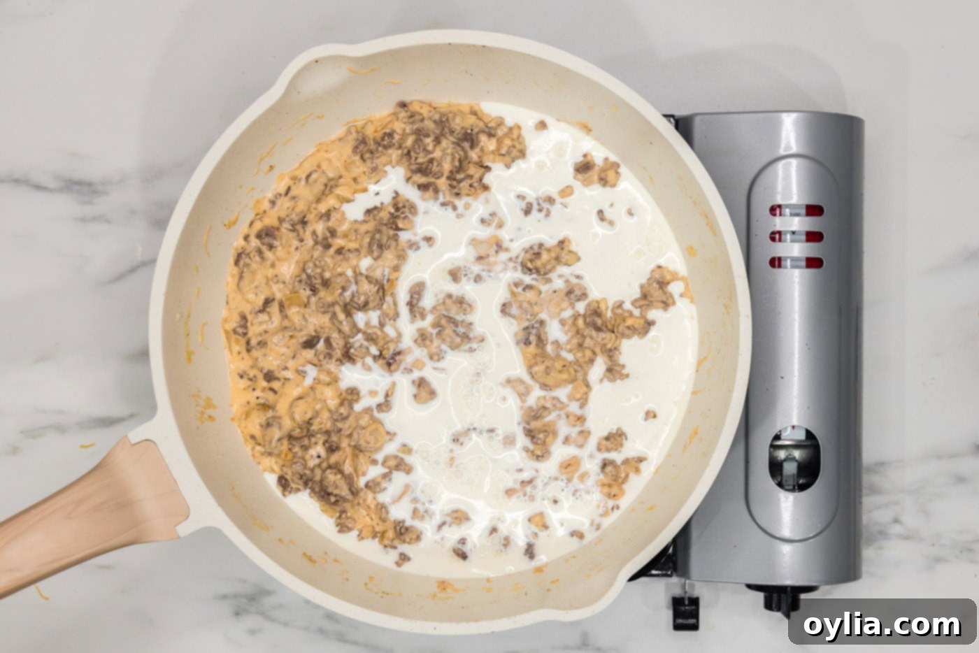 Pouring the remaining heavy cream into the cheesy beef and onion mixture to achieve the perfect dip consistency.