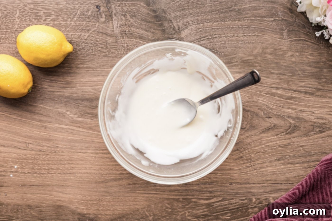 Smooth, bright lemon icing mixed in a small bowl with a spoon, ready for drizzling onto the cooled streusel squares.