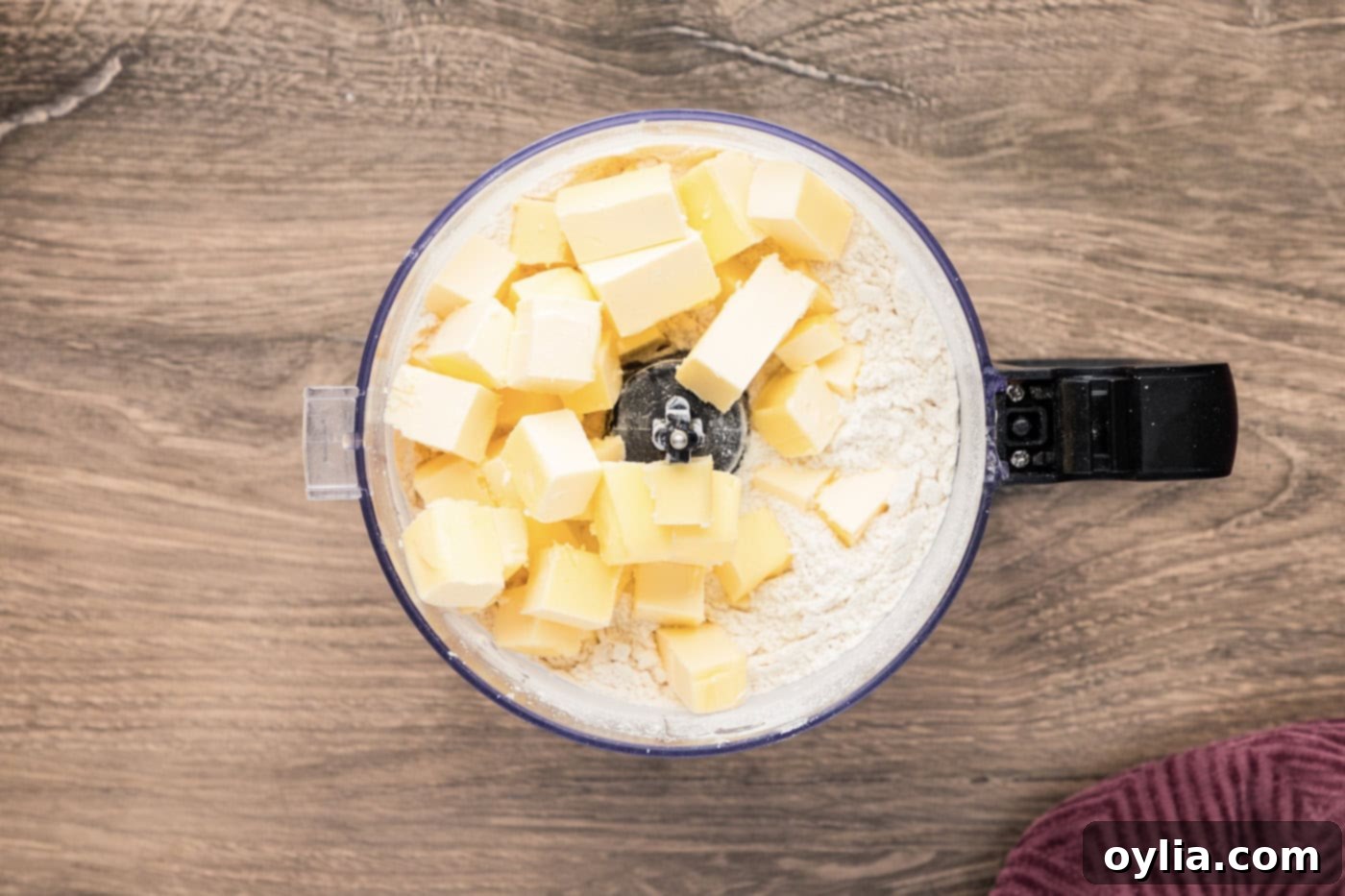 Cold butter cubes being added to the flour and sugar mixture in a food processor bowl, ready for processing into shortbread dough.