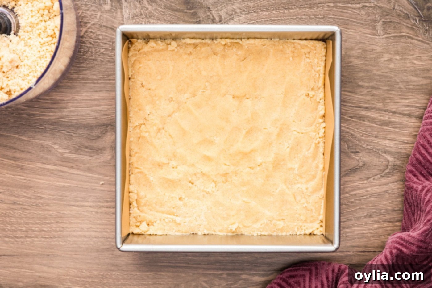The shortbread crumb mixture evenly pressed into a 9x9 baking pan, forming a solid, uniform base for the lemon streusel squares.