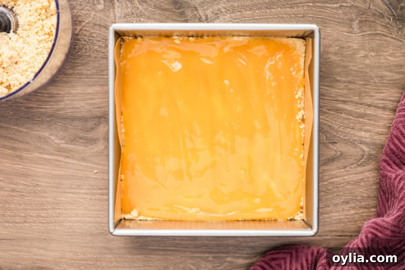 A smooth, vibrant layer of tangy lemon curd being spread over the buttery shortbread crust in the baking pan.