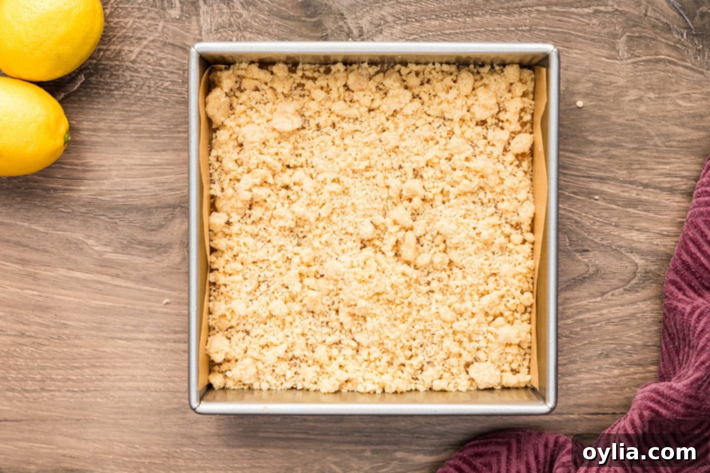 The reserved shortbread crumb mixture being sprinkled generously over the lemon curd layer, forming the streusel topping.