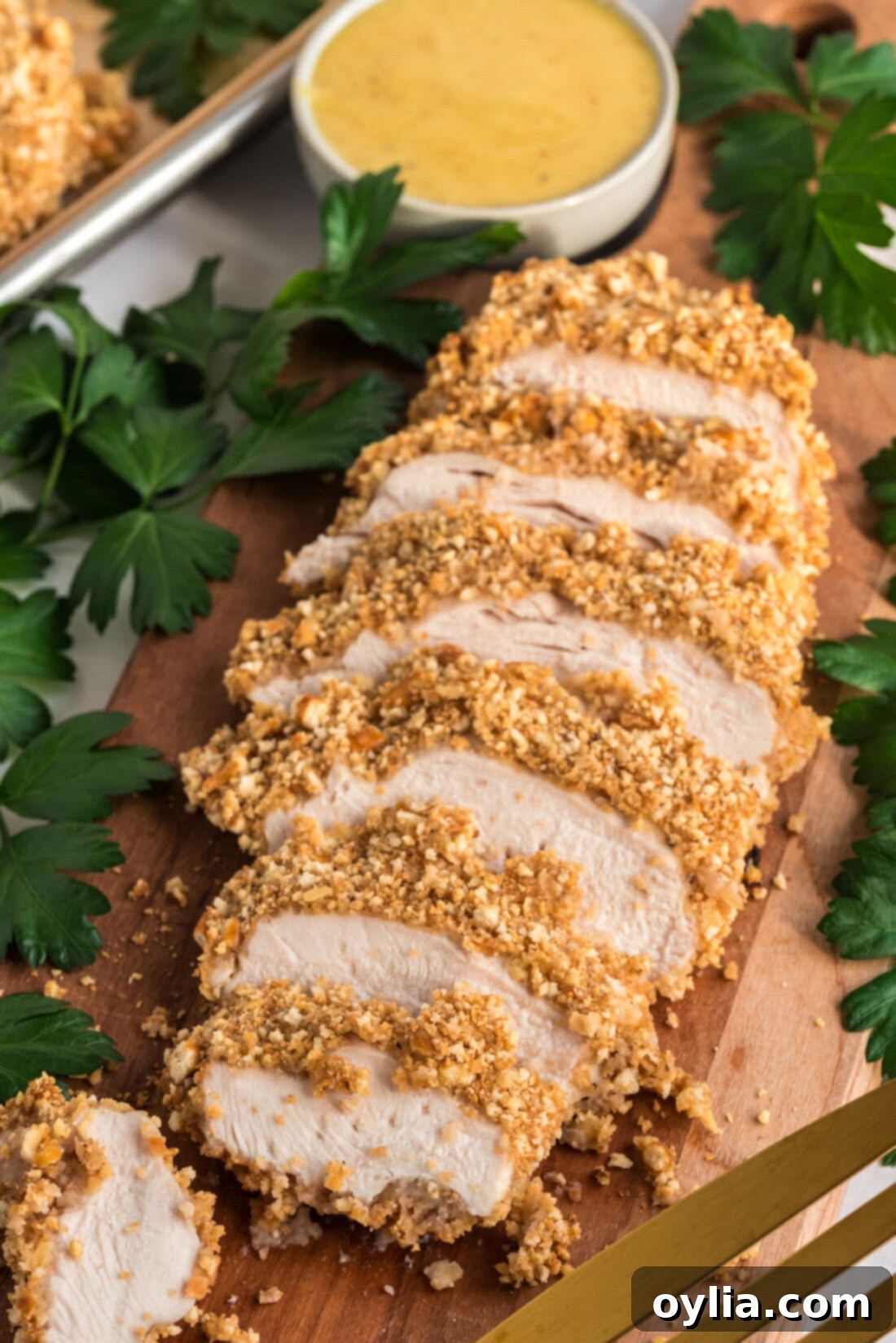 Sliced Pretzel Chicken on a wooden board, showcasing its golden, crunchy crust and tender interior, with a small bowl of honey mustard dressing nearby.