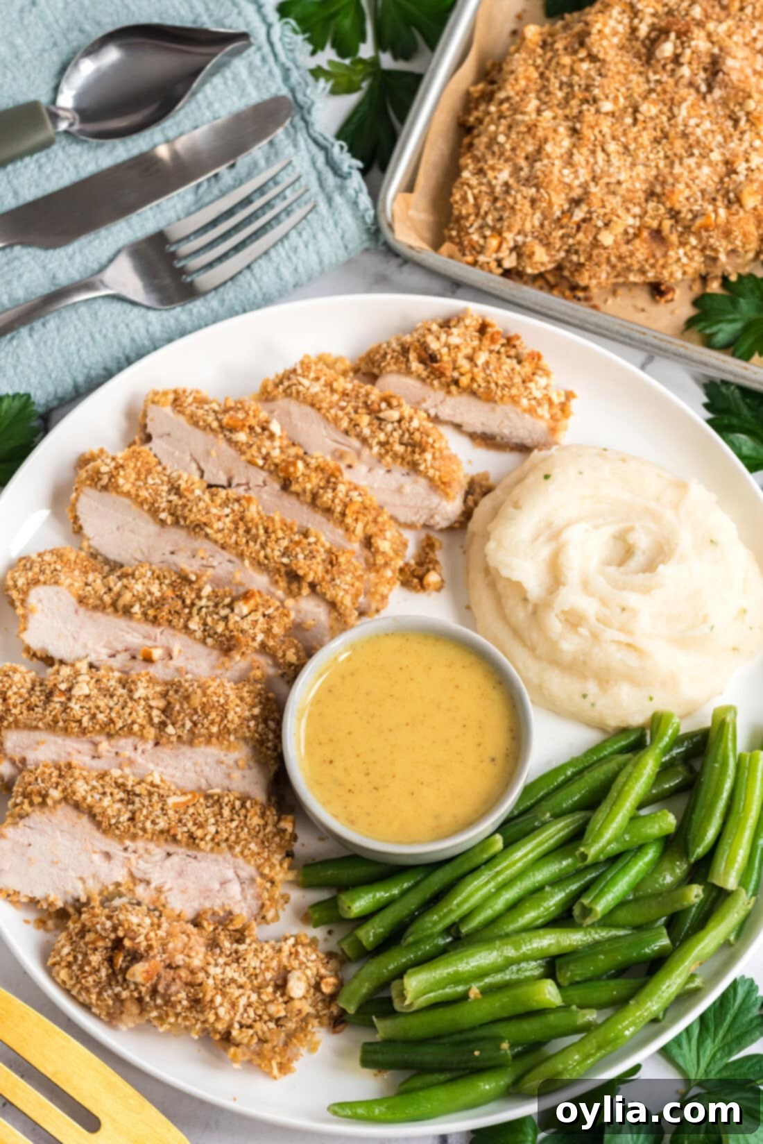 Sliced Pretzel Chicken plated with creamy mashed potatoes and vibrant green beans, showing a complete and balanced meal.